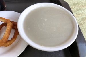 Bowl of grey-beige Beijing douzhier fermented mung bean juice served with fried dough rings and pickles