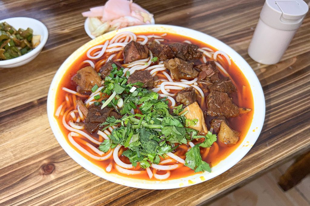 Bowl of Guizhou-style braised beef rice noodles in reddish broth, a related Guiyang-region noodle scene for changwang travellers