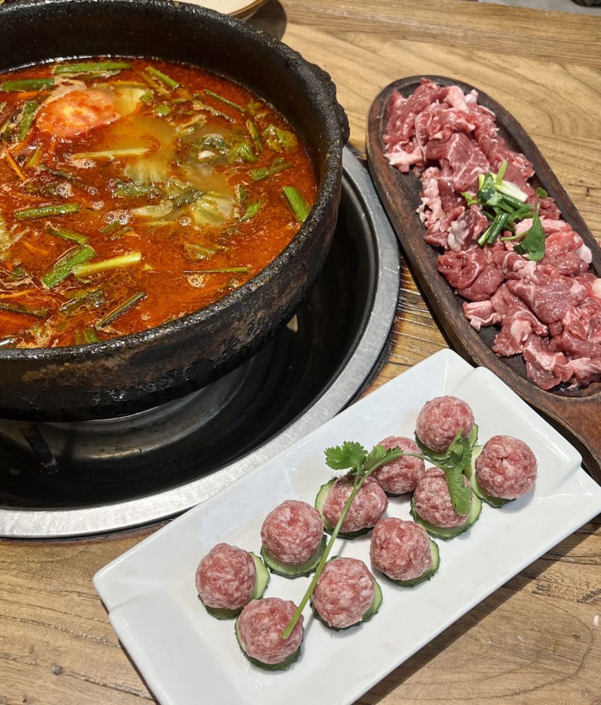 Guizhou Miao-style sour soup hotpot with red tomato broth, sliced beef, and meatballs on a wooden table