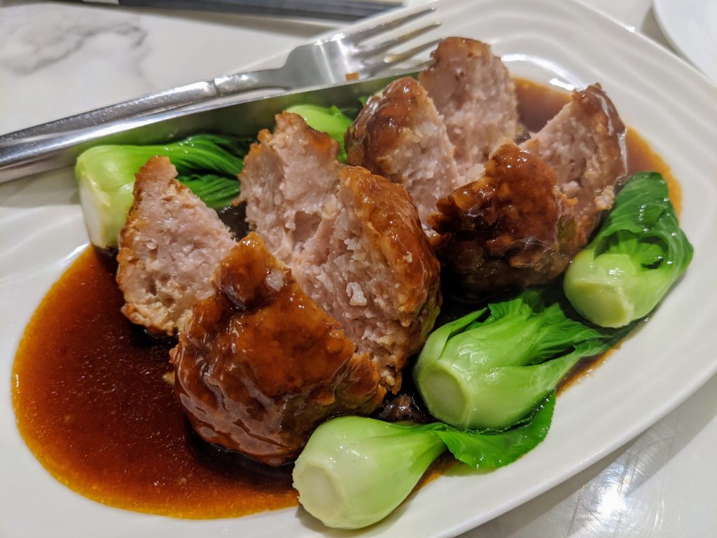 Large Jiangsu lion's head pork meatballs in brown braising sauce with greens
