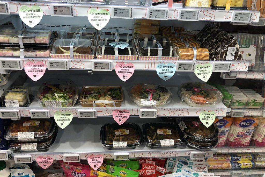 Chilled shelves of boxed bento meals and rice dishes with price tags at a JD convenience store in Beijing