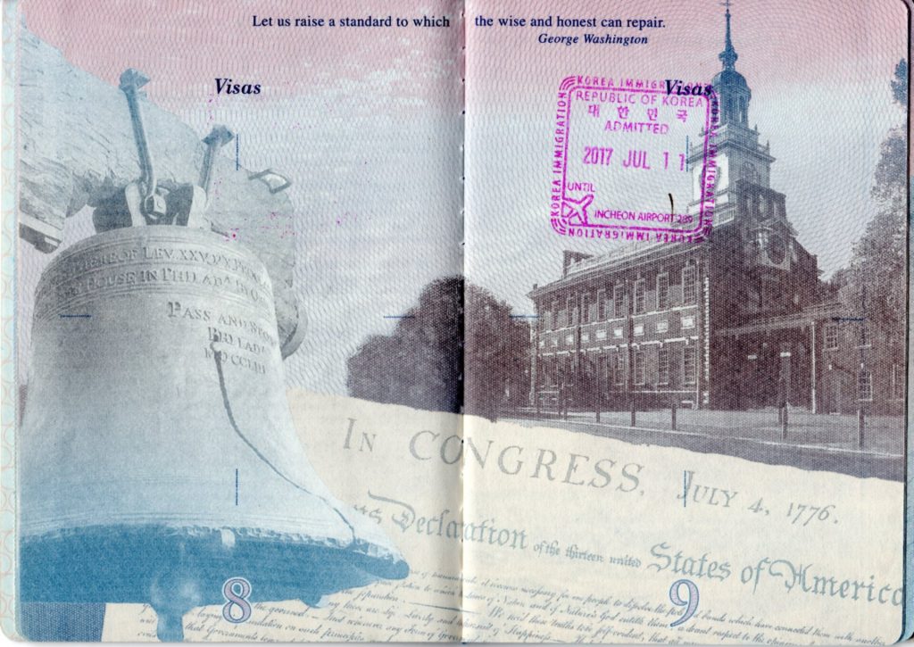 Open passport with visa stamps and blank pages on a wooden desk