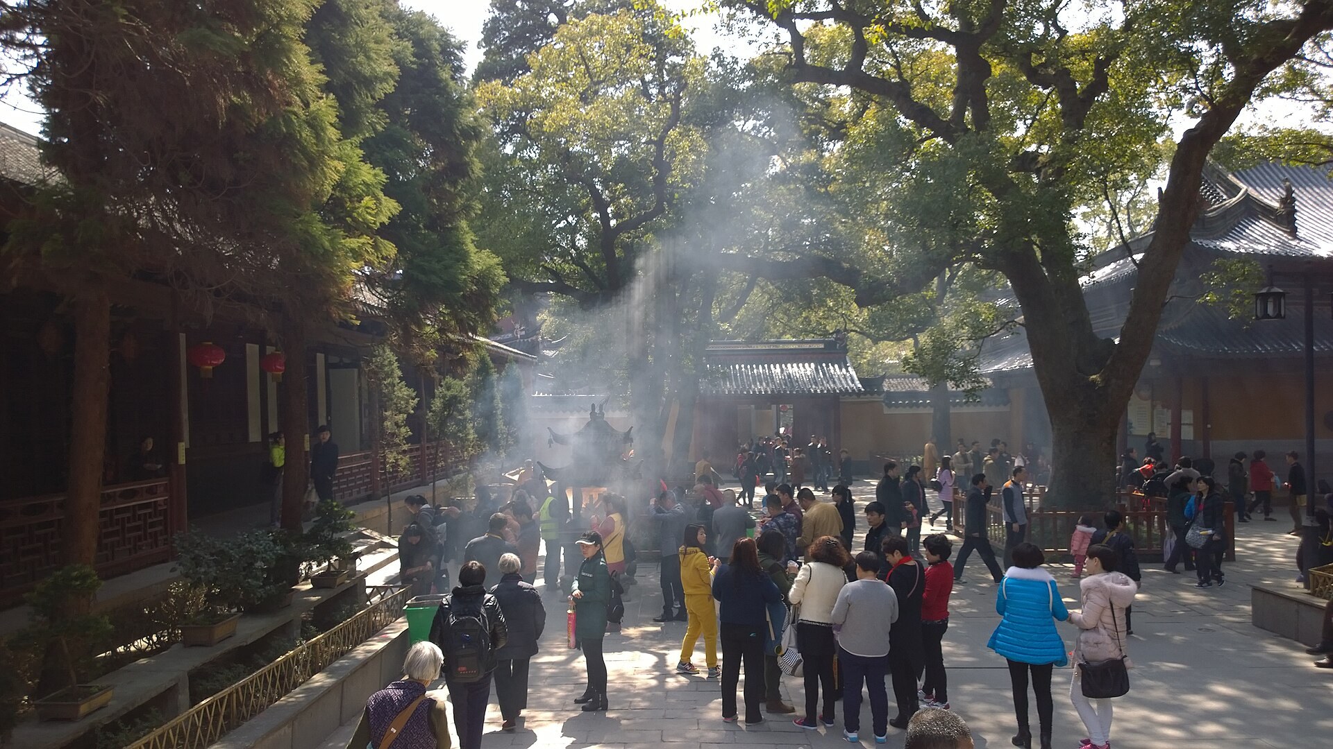 Temple courtyard with incense smoke rising beside red prayer ribbons