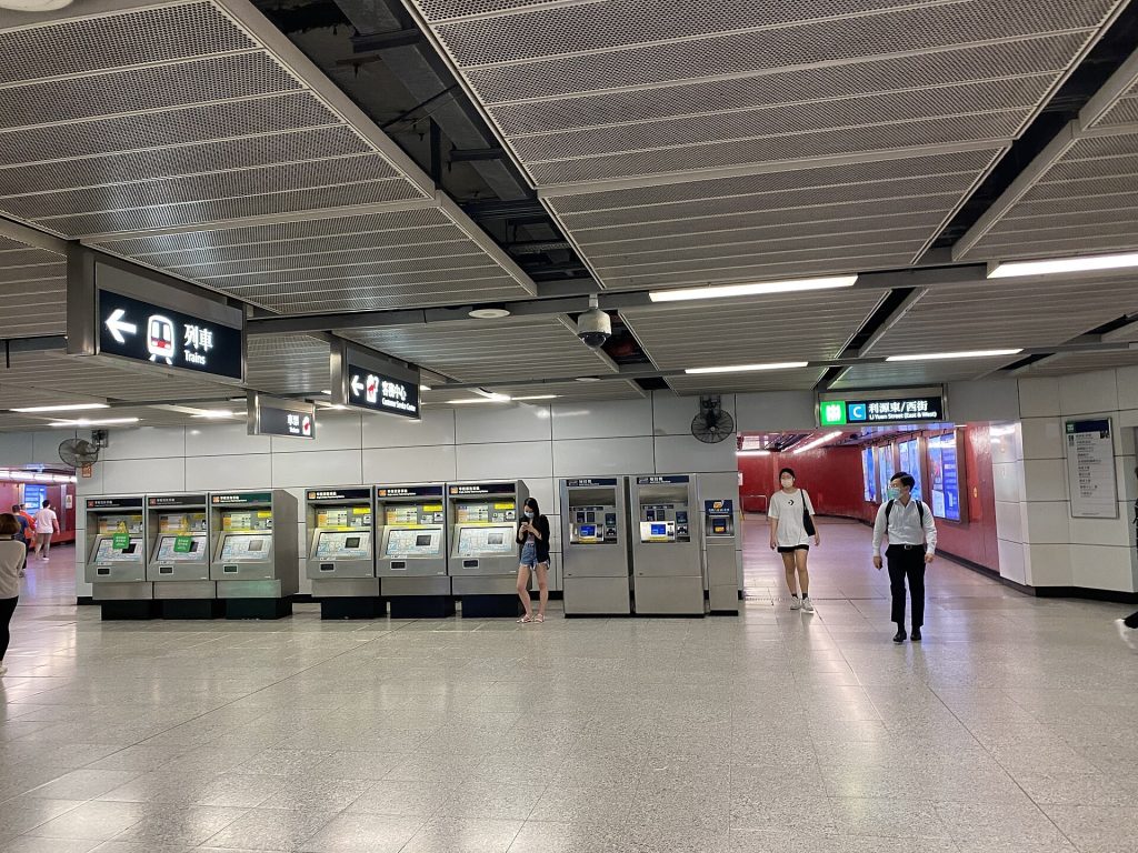 Travellers using self-service ticket machines inside a busy railway station hall