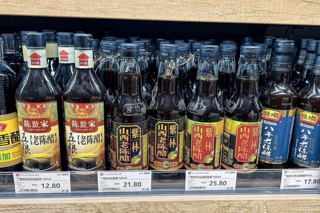 Supermarket shelf in Beijing lined with bottles of Shanxi mature vinegar from several brands, with price tags below