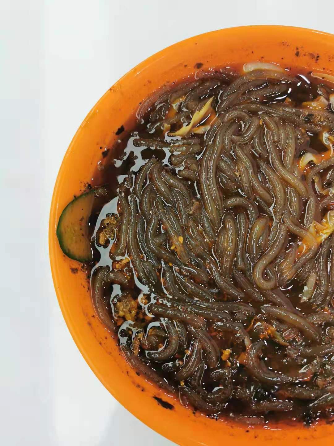 Close-up of a bowl of suanlafen with translucent sweet potato glass noodles in a dark, chili-oil and vinegar broth