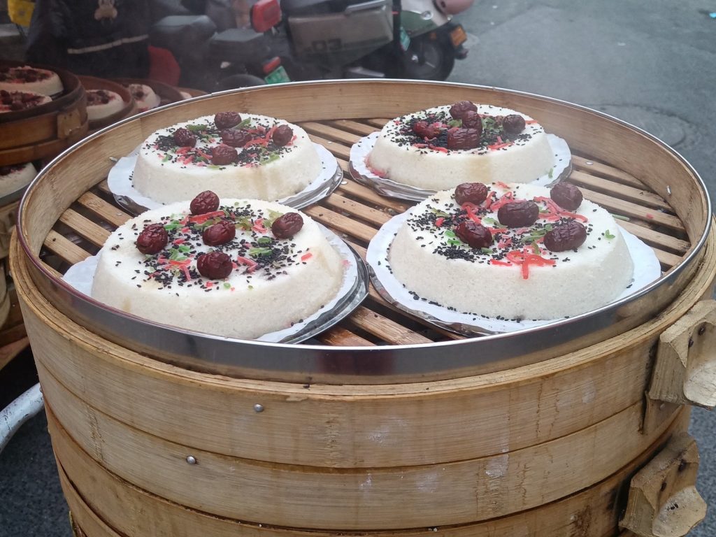 Round Chongyang cakes topped with red jujubes and nuts in a bamboo steamer