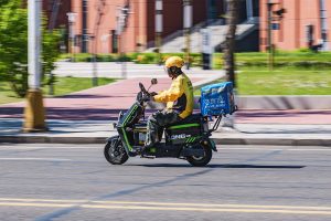 Food delivery worker in Meituan costume carrying an Ele.me box on a city street in Daqing