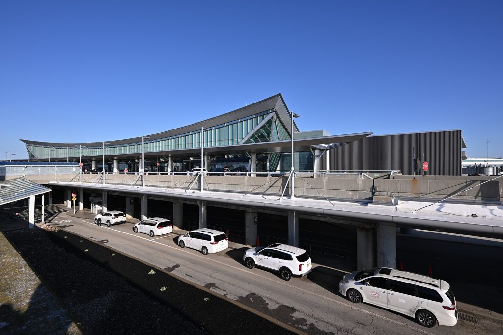 Ride-hailing sedan waiting at an airport arrivals curb with luggage carts nearby
