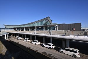 Ride-hailing sedan waiting at an airport arrivals curb with luggage carts nearby