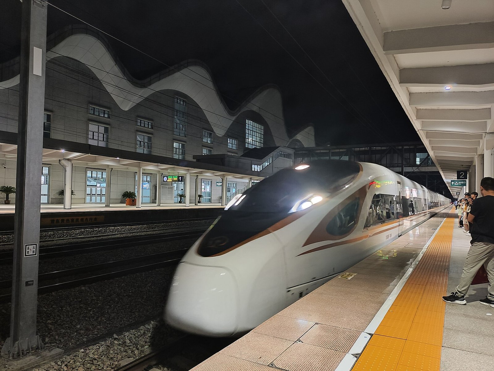 White Fuxing CR400BF high-speed train pulling into a lit station platform at night in Zhejiang