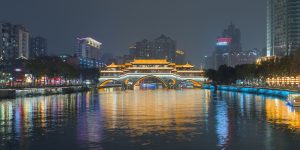 Anshun Bridge lit in gold at night over the Jin River in Chengdu, with colourful city lights reflected in the water