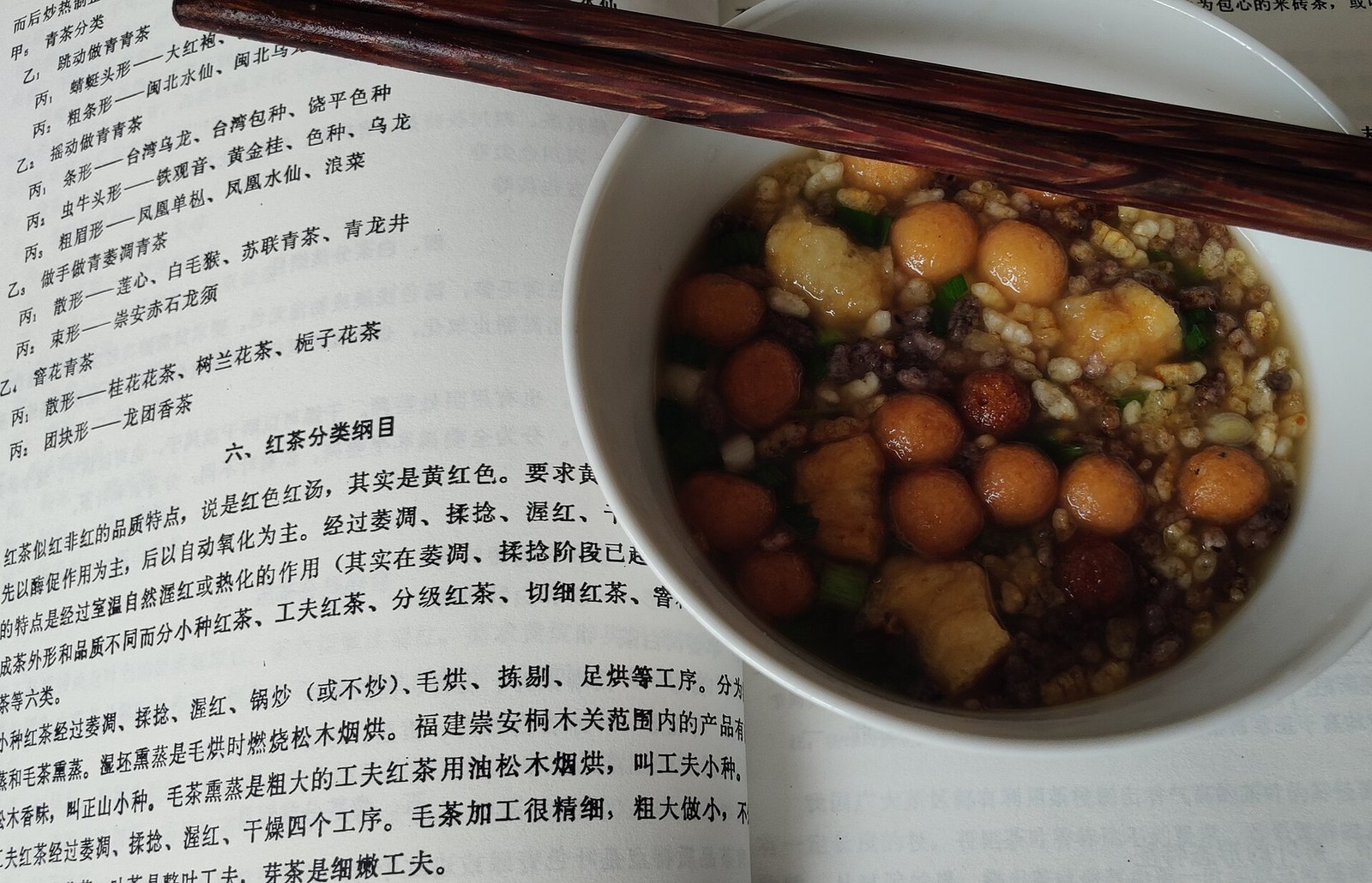 White bowl of Guangxi oil tea (youcha) topped with puffed rice, fried dough balls and chopped spring onion, with chopsticks resting on the rim