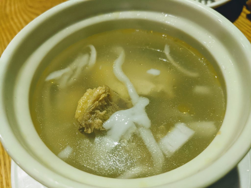 Bowl of Hainanese coconut chicken soup with chicken pieces in pale coconut broth