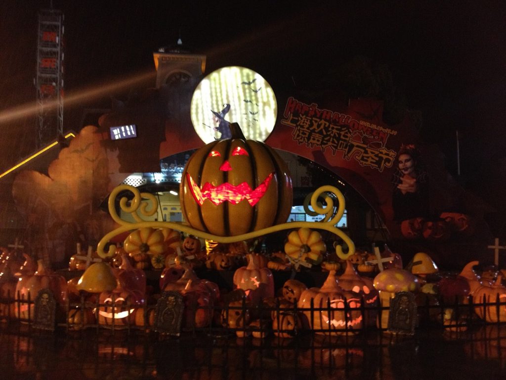 Giant glowing jack-o'-lantern pumpkin carriage and rows of carved pumpkins at the night-time Halloween entrance display of Shanghai Happy Valley theme park