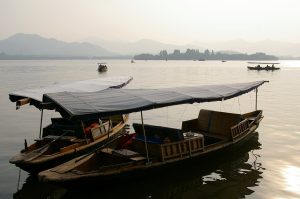 Traditional boats on Hangzhou West Lake with willow trees along the shore