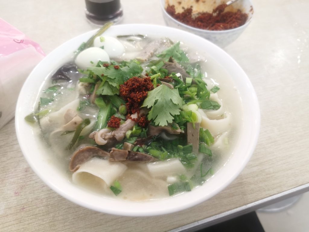 Bowl of Henan-style huimian braised noodles with wide hand-pulled noodles, broth, and toppings