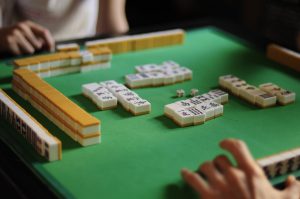 Players seated around a mahjong table with tiles laid out for a game