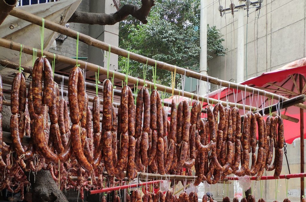 Rows of home-style Sichuan sausages and cured meat hanging from bamboo poles at a roadside stall in Chengdu, drying in the open air before Chinese New Year