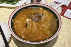 Bowl of Nanning laoyou rice noodles with beef, sour bamboo shoots and fermented black beans in an orange, chili-flecked broth