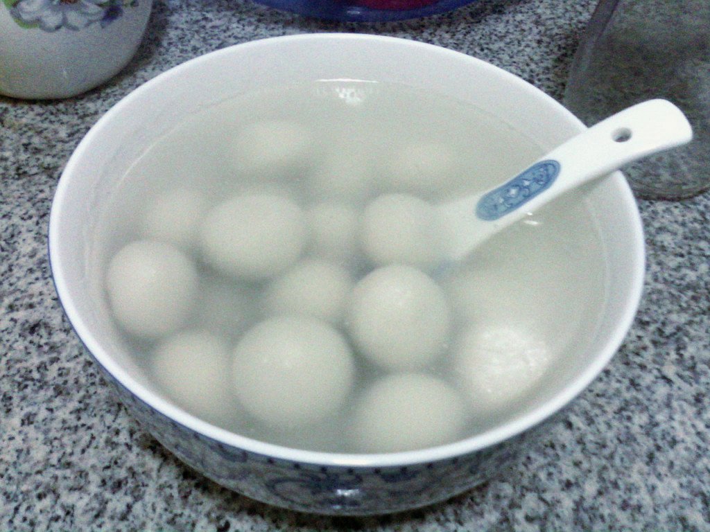 Bowl of white black-sesame tangyuan glutinous rice balls in clear sweet soup with a porcelain spoon