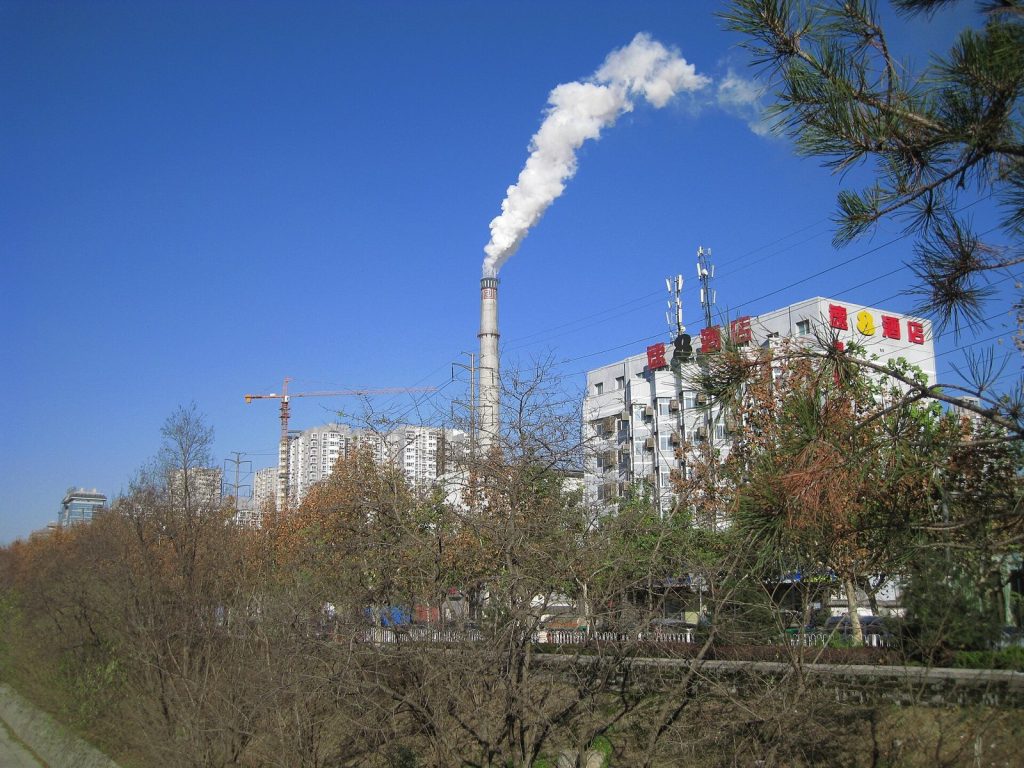 White steam rising from a district heating plant chimney beside apartment blocks in Xi'an on a clear winter day