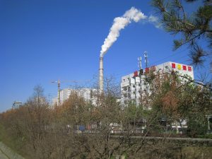 White steam rising from a district heating plant chimney beside apartment blocks in Xi'an on a clear winter day