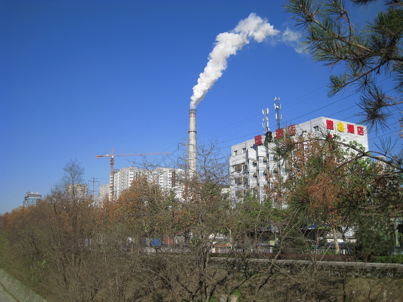 White steam rising from a district heating plant chimney beside apartment blocks in Xi'an on a clear winter day