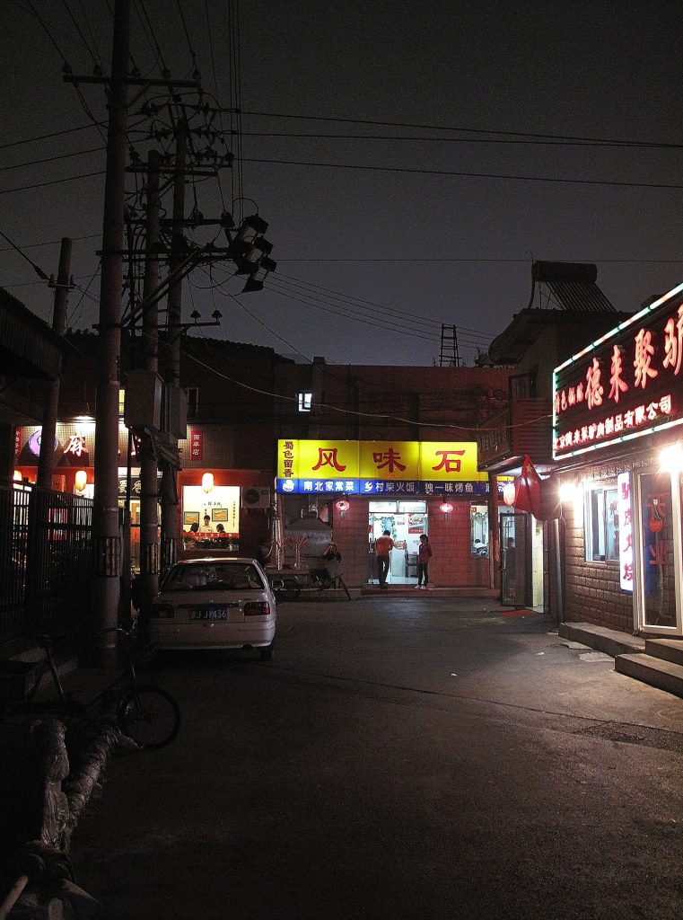 Narrow Beijing hutong alley with glowing doorway lights at dusk