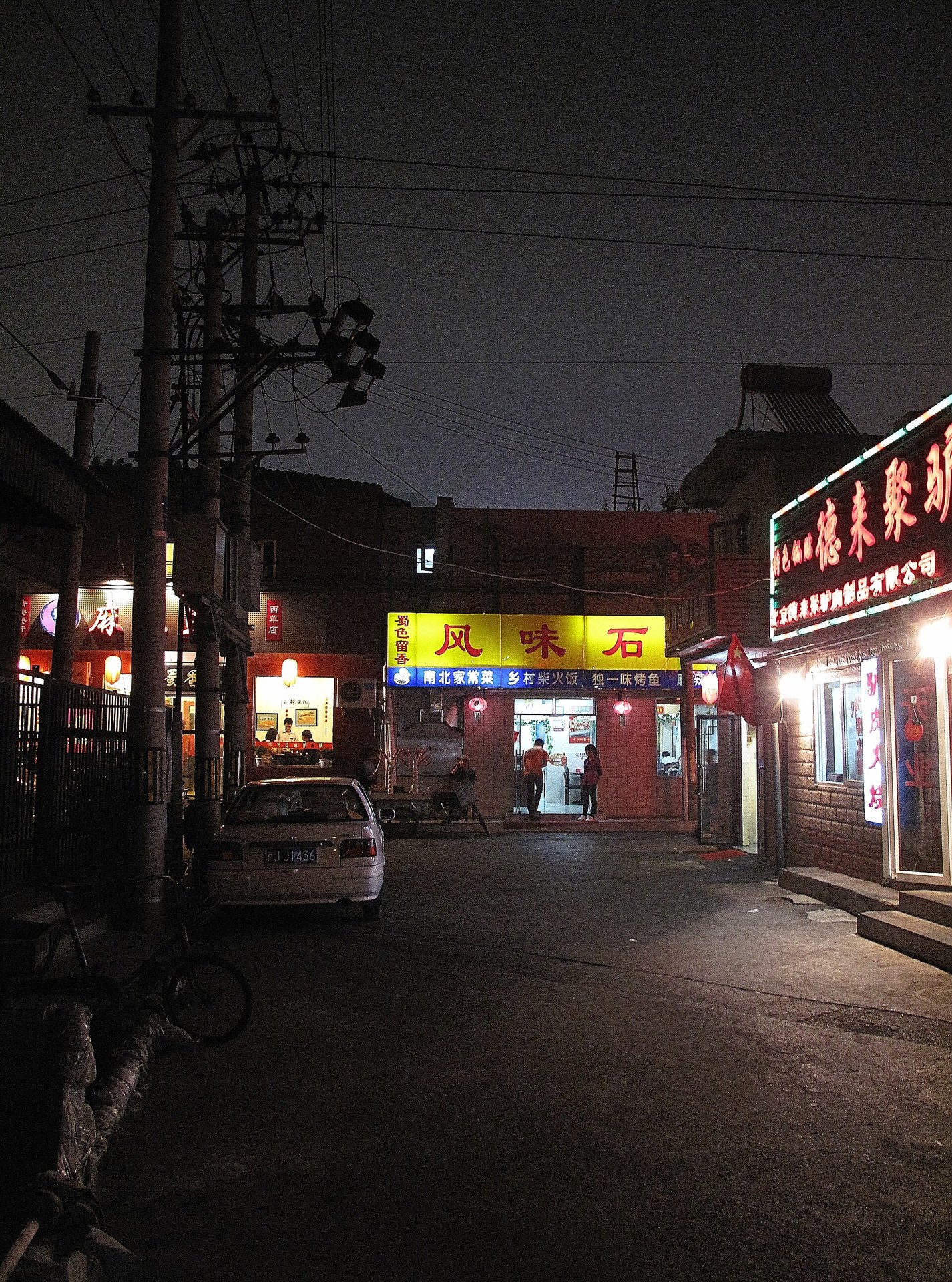 Narrow Beijing hutong alley with glowing doorway lights at dusk