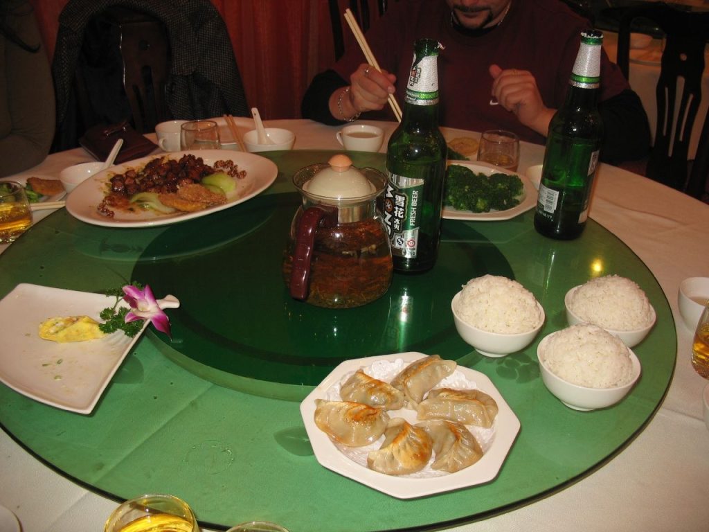 Shared Chinese dishes on a lazy Susan in a busy restaurant
