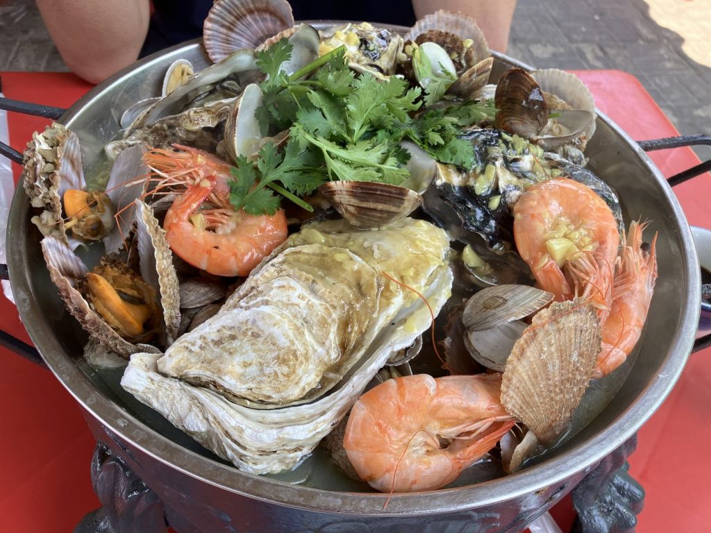 Large platter of mixed Qingdao-style seafood with oysters, shrimp, scallops, clams, garlic and coriander on a red outdoor table