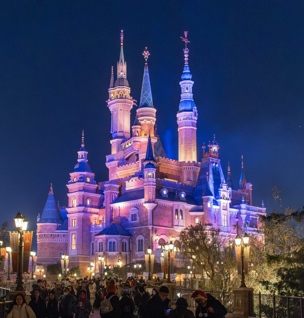 Amusement park castle and promenade with visitors under daytime sky